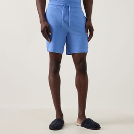 Model wearing Hugo Austin Waffle-Knit Logo Lounge Shorts in Bright Blue, mid-rise with drawstring waist, styled with navy slippers