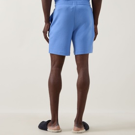Model wearing Hugo Austin Waffle-Knit Logo Lounge Shorts in Bright Blue, rear view, styled with navy slip-on sandals.