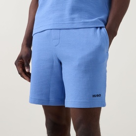 Model wearing Hugo Austin Waffle-Knit Logo Lounge Shorts in Bright Blue, styled with matching blue top. Waffle texture and contrast logo visible.