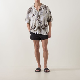 Model wearing Hugo Light Beige viscose shirt with butterfly print, styled with black swim shorts and dark slide sandals