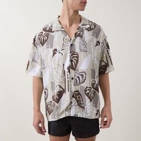 Model wearing Hugo light beige viscose shirt with brown and green tropical leaf print, short sleeves and camp collar, styled with black shorts