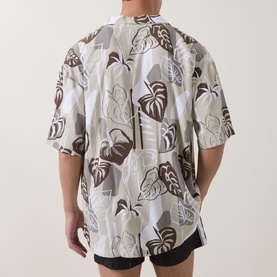 Model wearing Hugo light beige short-sleeve shirt with brown and white tropical leaf print, styled with black shorts, rear view