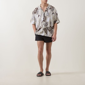 Model wearing Hugo light beige viscose shirt with tropical leaf print, styled with black swim shorts and dark slider sandals.