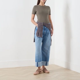 Model wearing Mother straight jeans in Last Bite light blue denim with deep cuffs, styled with olive tee and striped shirt tied at waist
