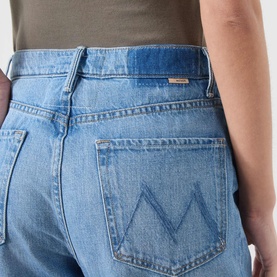 Model wearing Mother Straight Jeans in Last Bite light blue wash, close-up of back pocket with embroidered M logo detail.