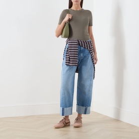 Model wearing Mother straight jeans in Last Bite light blue denim with deep cuffed hem, styled with khaki tee and striped shirt tied at waist.