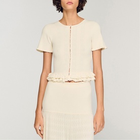 Model wearing Sandro Ruffle Knit Cardigan in clear, cropped with pearl buttons and short ruffled sleeves, styled with a matching knit skirt.