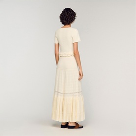 Model wearing Sandro Ruffle Knit Cardigan in clear, styled with a matching cream maxi skirt and dark flat shoes, rear view.