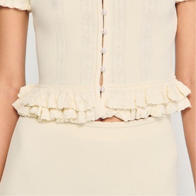 Model wearing Sandro Ruffle Knit Cardigan in clear, showing cropped back view with layered ruffle hem and pearl button fastening detail.