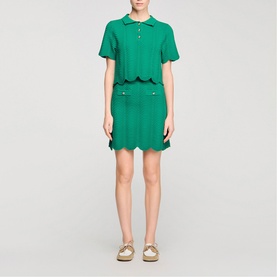 Model wearing Sandro Scallop Trim Knitted Skirt in emerald green with matching polo top and gold slide sandals.