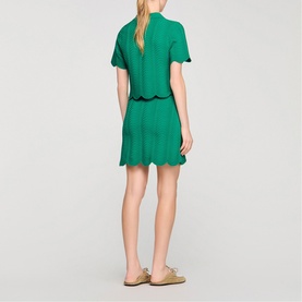 Model wearing Sandro Scallop Trim Knitted Skirt in emerald green with matching top, scalloped hem detail, styled with gold sandals.
