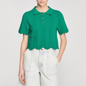 Model wearing Sandro Scallop Trim Knitted Top in emerald green with polo collar and gold buttons, styled with light-wash jeans.