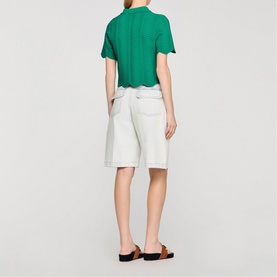 Model wearing Sandro Scallop Trim Knitted Top in emerald green with scallop hem, styled with white denim shorts and tan sandals, back view.