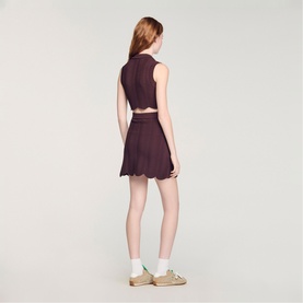 Model wearing Sandro Wave Cropped Knit Top in brown, sleeveless with polo collar, styled with matching mini skirt and cream trainers.