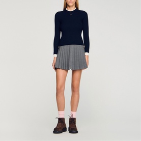 Model wearing Sandro Layered Effect Ribbed Sweater in navy blue with white collar and cuffs, styled with grey pleated mini skirt and brown boots.