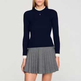 Model wearing Sandro Layered Effect Ribbed Sweater in navy blue with white contrast collar and cuffs, styled with grey pleated mini skirt.
