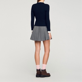Model wearing Sandro Layered Effect Ribbed Sweater in navy blue with contrasting white collar and cuffs, styled with grey pleated mini skirt and