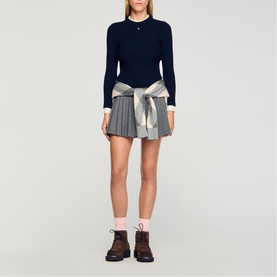 Model wearing Sandro Layered Effect Ribbed Sweater in navy blue with contrasting cuffs and collar, styled with grey pleated mini skirt and plaid