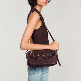 Model carrying Sandro Le Mambo Janys Studded Suede Bag in black brown, gold studs and logo buckles, worn crossbody with adjustable strap.