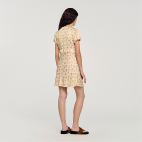 Model wearing Sandro Floral Ruffle Mini Dress in light pink with floral print, short sleeves, and V-neckline, styled with tan slides.