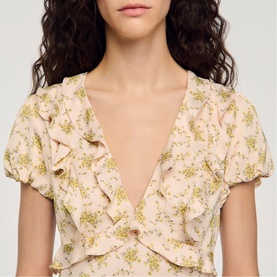 Model wearing Sandro Floral Ruffle Mini Dress in light pink with green floral print, V-neckline, ruffled detail, and short sleeves