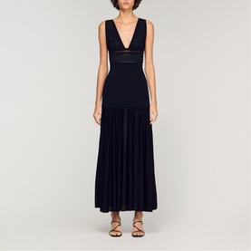 Model wearing Sandro Embroidered Hybrid Dress in black, featuring deep V-neckline, fitted waist, and pleated maxi skirt, styled with strappy sandals.