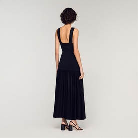 Model wearing Sandro Embroidered Hybrid Dress in black, shown from behind, with deep scoop back and pleated maxi skirt, styled with black heeled