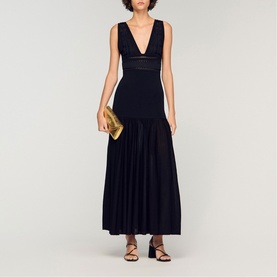 Model wearing Sandro Embroidered Hybrid Dress in black, deep V-neck, pleated maxi skirt, styled with gold clutch and strappy heels.