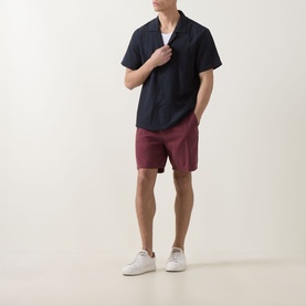 Model wearing Hugo Boss black short-sleeve shirt with camp collar, styled with burgundy shorts and white trainers.