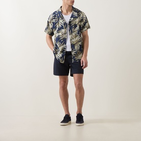 Model wearing Hugo Boss dark beige tropical leaf print short-sleeve shirt, styled with navy shorts and navy canvas shoes.