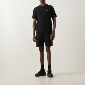 Model wearing Hugo Boss black cotton shorts with side stripe detail, styled with matching black T-shirt and black chunky trainers.