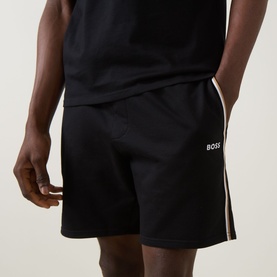 Model wearing Hugo Boss black cotton lounge shorts with white side stripe and BOSS logo, styled with matching black vest top