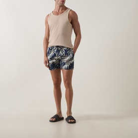 Model wearing Hugo Boss Dark Beige swim shorts with tropical leaf print, styled with a beige vest and black slider sandals.