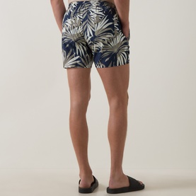 Model wearing Hugo Boss dark beige tropical palm leaf print swim shorts, styled with black slider sandals, rear view.