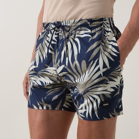 Model wearing Hugo Boss dark beige tropical palm print swim shorts with elasticated waist and gold logo badge