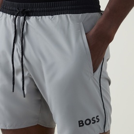 Model wearing Hugo Boss Starfish Logo Swim Shorts in grey with black contrast piping, elasticated waist, drawstring, and side pockets.