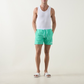 Model wearing Hugo Boss bright green swim shorts with white drawstring waistband, styled with a white vest and white slider sandals.