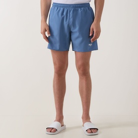Model wearing Hugo Boss Swordfish Logo Swim Shorts in light pastel blue with elasticated waistband and logo detail, styled with white slides.