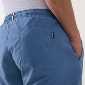 Model wearing Hugo Boss Swordfish Logo Swim Shorts in light blue, showing rear patch pocket, elasticated waistband and BOSS logo tab detail.