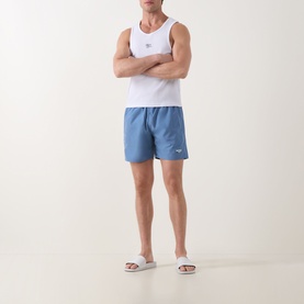 Model wearing Hugo Boss Swordfish Logo Swim Shorts in light pastel blue, styled with a white vest and white slider sandals