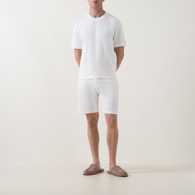 Model wearing Hugo Boss Structure Logo Textured Lounge Shorts in Natural, paired with matching white textured T-shirt and taupe slip-on shoes.
