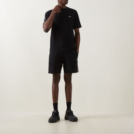 Model wearing Hugo Boss black cotton T-shirt with matching black shorts, white side stripe, and chunky black trainers.