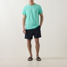 Model wearing Hugo Boss bright green cotton T-shirt with navy swim shorts and dark slider sandals