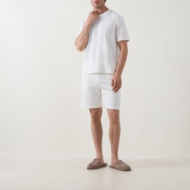 Model wearing Hugo Boss Structure Logo Textured Lounge T-Shirt in Natural, styled with white lounge shorts and taupe slippers.