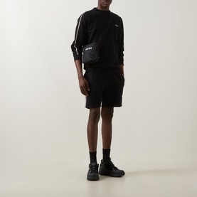 Model wearing Hugo Boss black cotton sweatshirt with white sleeve stripe, styled with matching black shorts and crossbody bag.