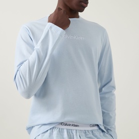 Model wearing Calvin Klein Logo Check Print Pyjama Set in Ballad Blue, long-sleeve top with tonal logo, check print bottoms visible at waist.