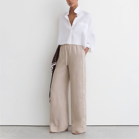 Model wearing Reiss beige wide-leg trousers with white shirt, carrying a brown bag over shoulder.