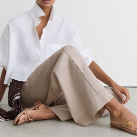 Model wearing Reiss beige wide-leg trousers, styled with a white oversized shirt and neutral flat sandals