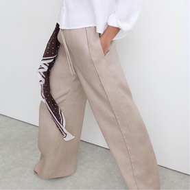 Model wearing Reiss beige wide-leg trousers with a brown polka dot scarf tied at the waist, styled with a white shirt.