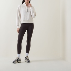 Model wearing Spanx Oatmeal Heather sweat top with half-zip neck, styled with dark brown leggings and grey trainers.